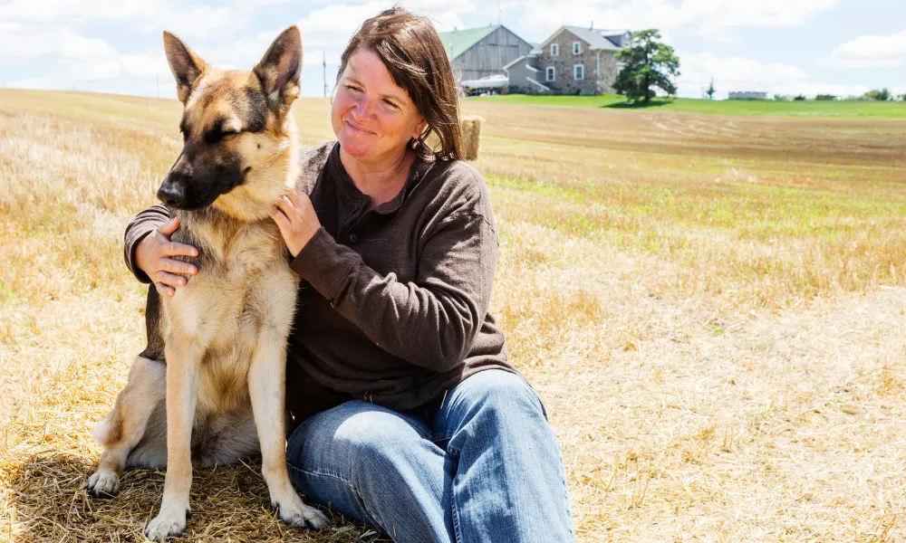 A woman in the countryside scratching the neck of her female German Shepherd.